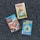 Three Nancy Drew mystery books are arranged on a textured gray carpet. The titles include 'The Secret of the Old Clock', 'The Broken Anchor', and 'Tall, Dark and Deadly'. Each book cover features distinct artwork related to the story.