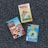 Three Nancy Drew mystery books are arranged on a textured gray carpet. The titles include 'The Secret of the Old Clock', 'The Broken Anchor', and 'Tall, Dark and Deadly'. Each book cover features distinct artwork related to the story.