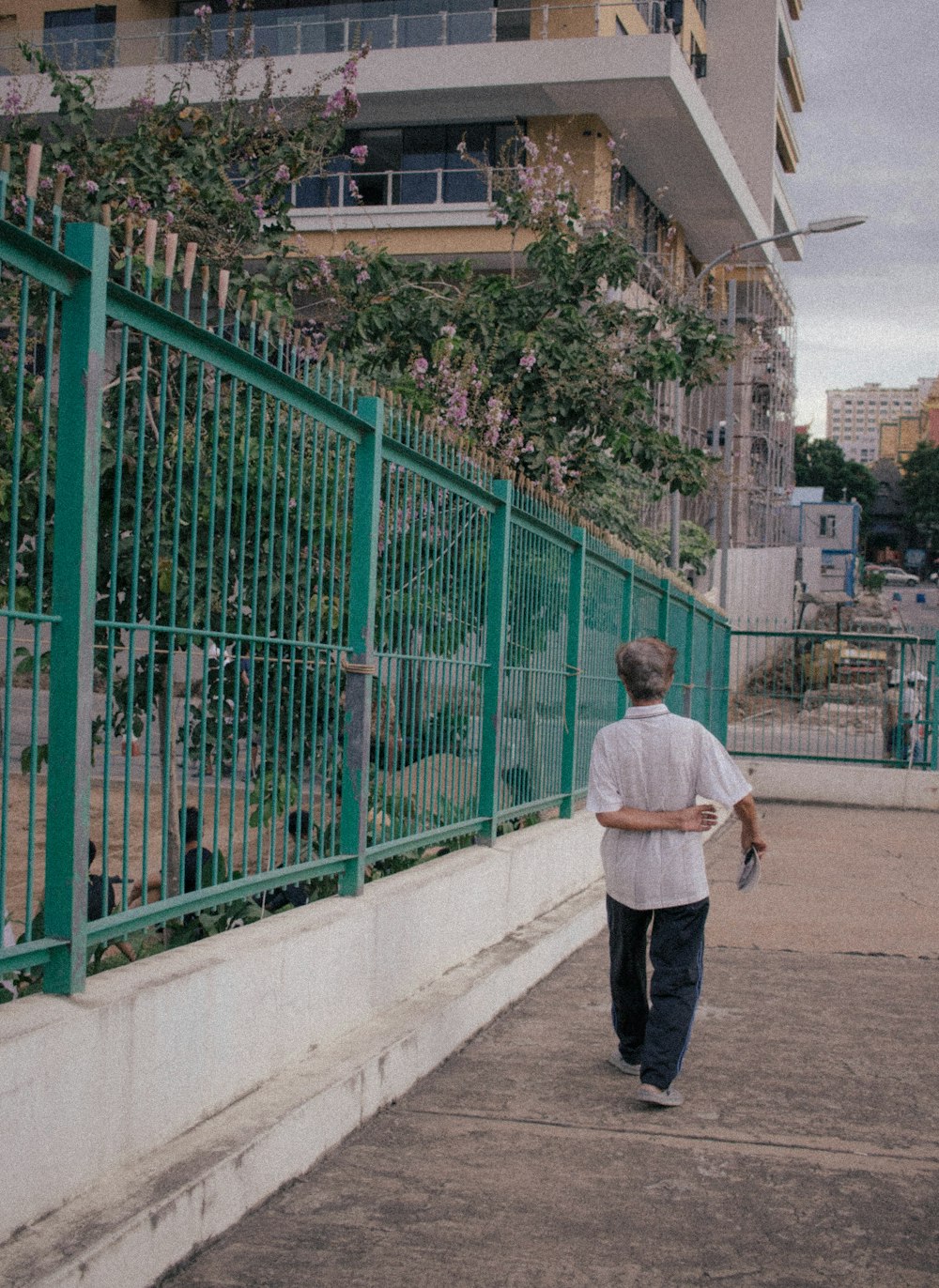 man in white dress shirt and black pants standing beside green metal fence during daytime