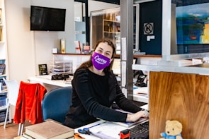 a woman sitting at a desk with a purple mask on her face