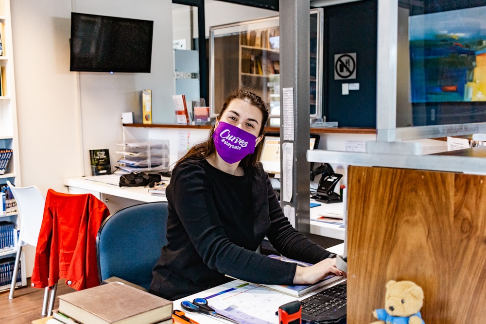 a woman sitting at a desk with a purple mask on her face