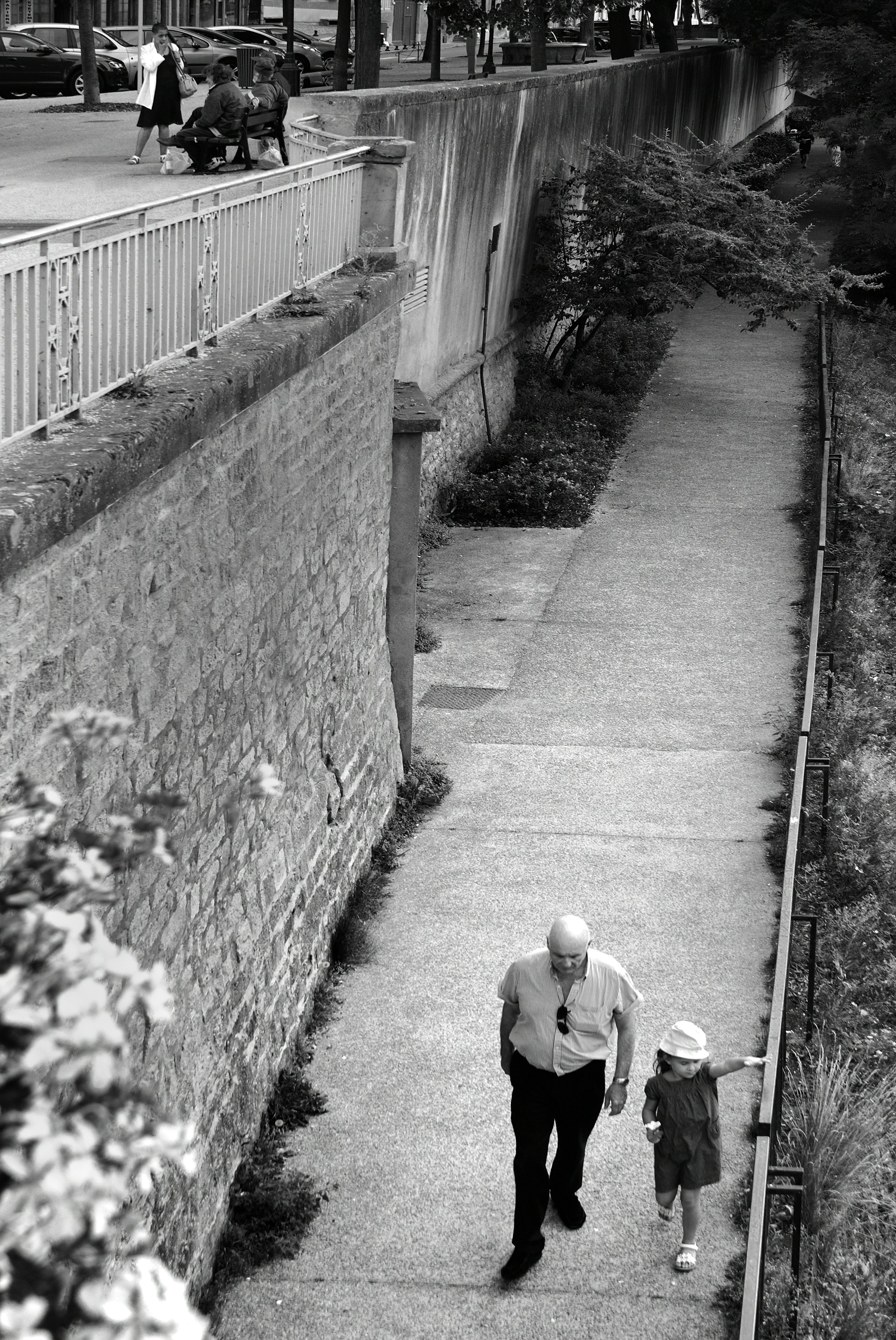 grayscale photo of man in black jacket and pants walking on pathway