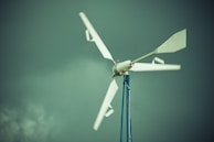 A wind turbine with white blades is mounted on a tall blue pole against a backdrop of a cloudy, greenish sky.