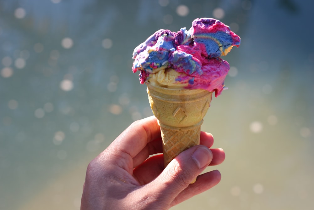 person holding ice cream cone with purple and pink ice cream