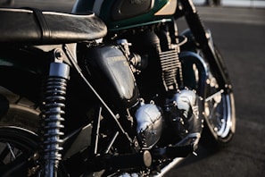A detailed view of a classic motorcycle, focusing on its engine and parts, with sunlight reflecting off the metallic surfaces. The bike's branding is visible on the engine casing, and the image captures a sense of craftsmanship and vintage appeal.