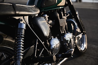 A detailed view of a classic motorcycle, focusing on its engine and parts, with sunlight reflecting off the metallic surfaces. The bike's branding is visible on the engine casing, and the image captures a sense of craftsmanship and vintage appeal.