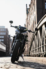 A shiny motorcycle parked on a cobblestone street under warm afternoon light.