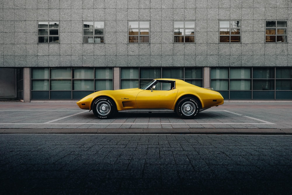 Porsche 911 amarillo aparcado cerca de un edificio de hormigón blanco