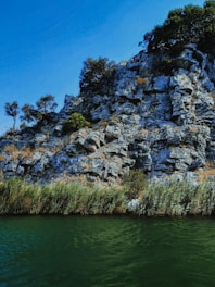 gray rocky mountain beside body of water during daytime