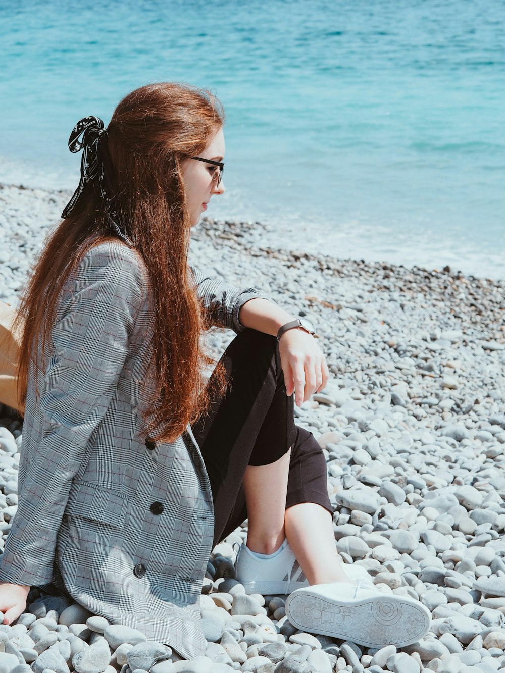 woman in white cardigan sitting on gray rocky shore during daytime