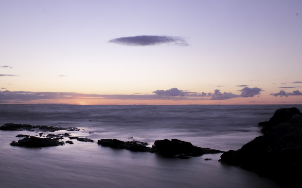 silhouette of rocks on sea shore during sunset