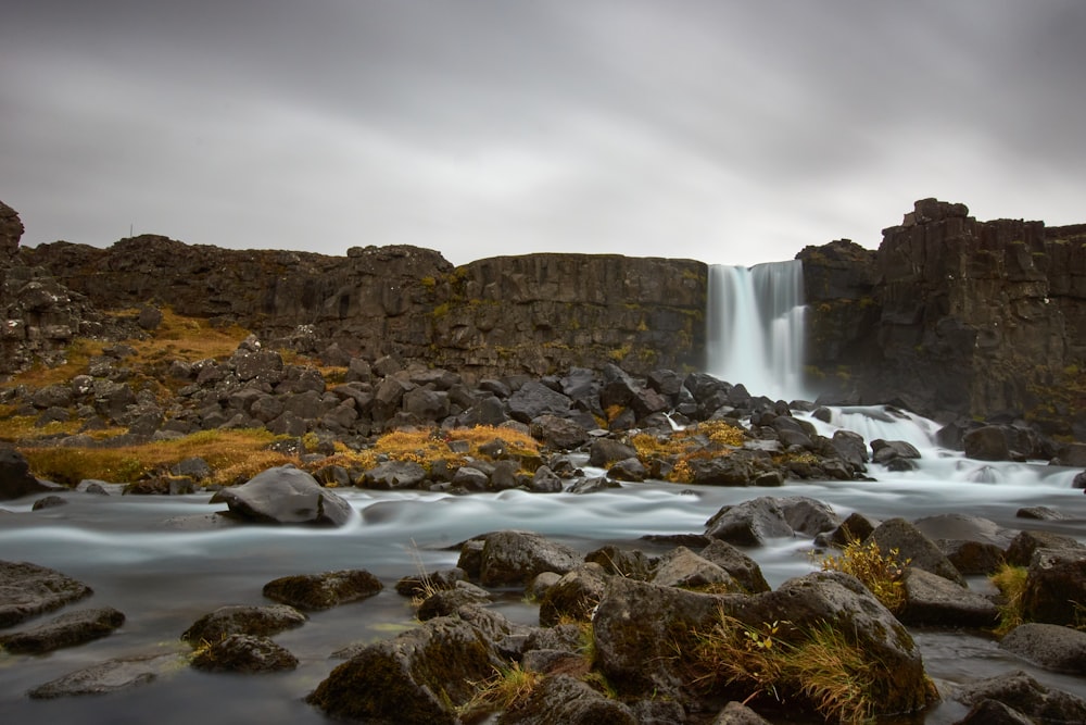 water falls on rocky shore under gray cloudy sky during daytime