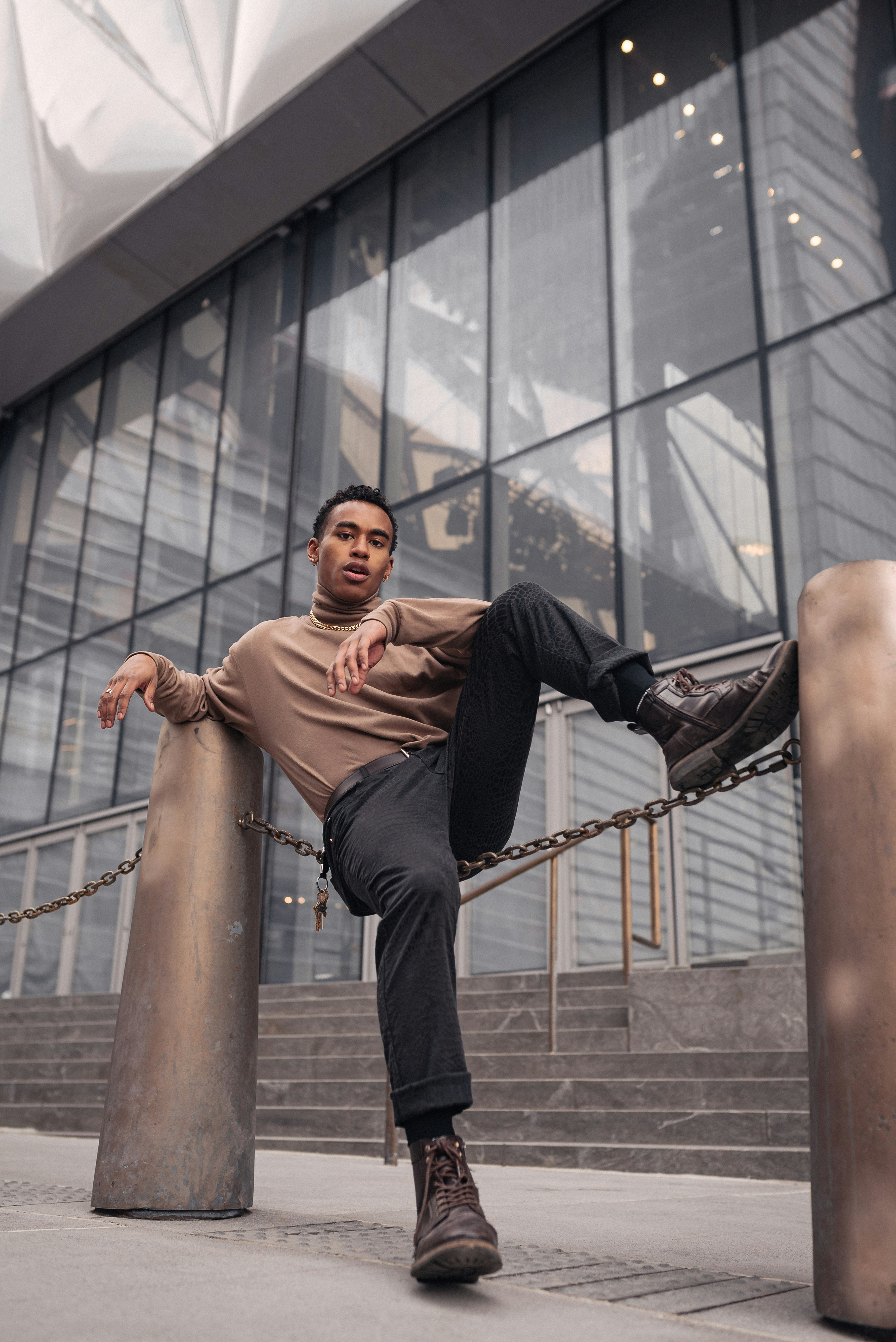 man in brown long sleeve shirt and black pants sitting on brown metal bar during daytime