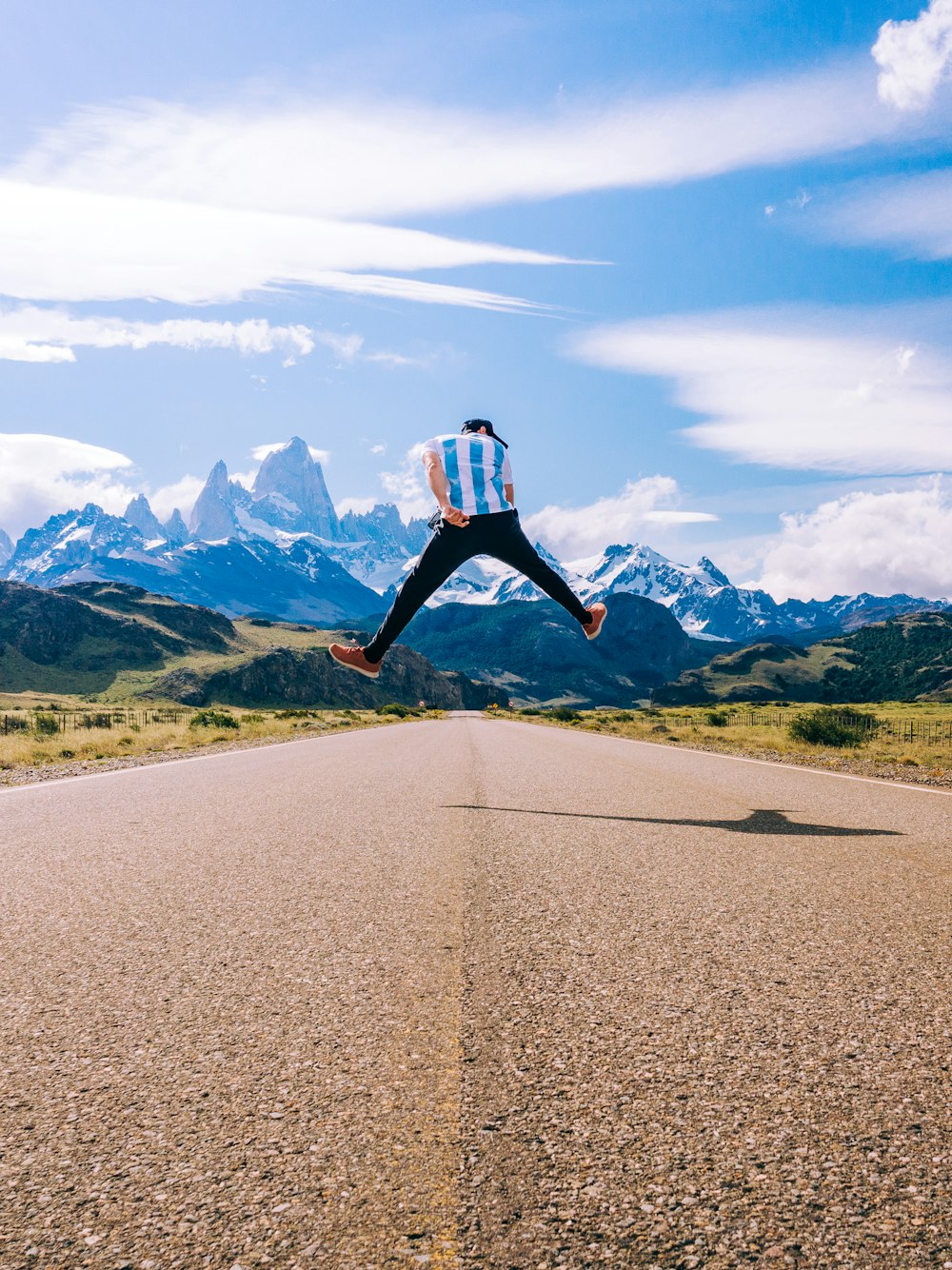 woman in black jacket and black pants jumping on gray asphalt road during daytime