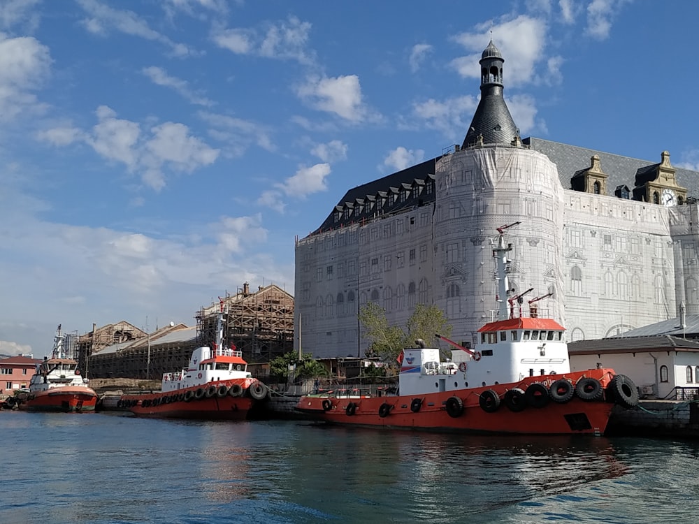 barco vermelho e branco na água perto do edifício de concreto cinzento durante o dia