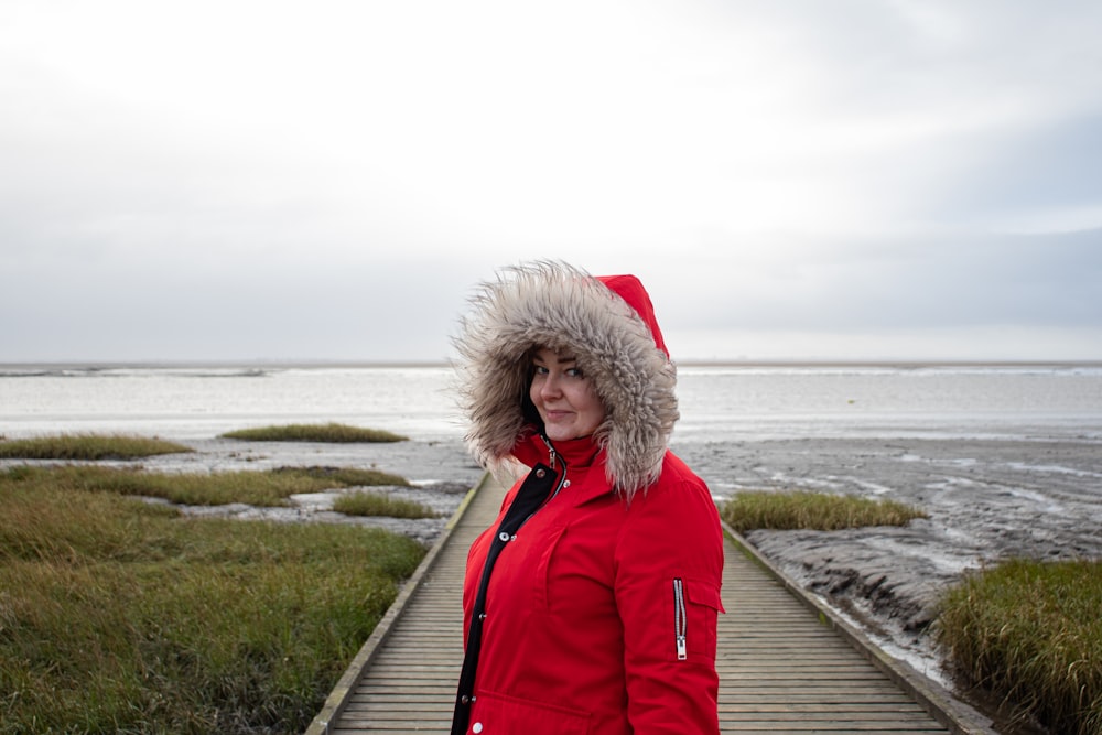 woman in red jacket standing on wooden dock during daytime