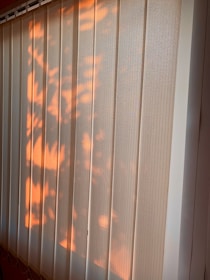 Vertical blinds partially illuminated by warm sunlight, casting soft, natural patterns and shadows across the surface.
