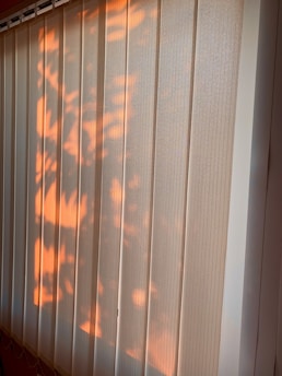Vertical blinds partially illuminated by warm sunlight, casting soft, natural patterns and shadows across the surface.