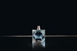Close-up of an elegant dark glass perfume bottle embossed with a crescent moon emblem, softly lit against a midnight blue velvet backdrop.
