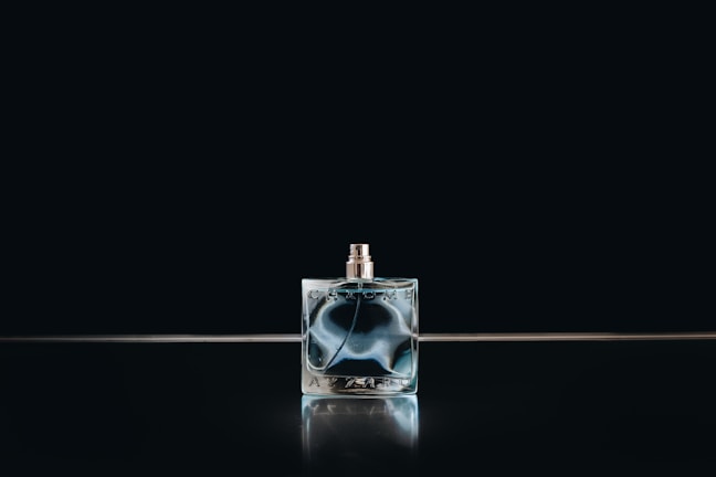 Close-up of an elegant dark glass perfume bottle embossed with a crescent moon emblem, softly lit against a midnight blue velvet backdrop.