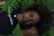 A person with closed eyes rests peacefully among green ferns, wearing a black shirt with the word 'champion' in white lettering. Their head is positioned on their arm, and they have a calm, serene expression.