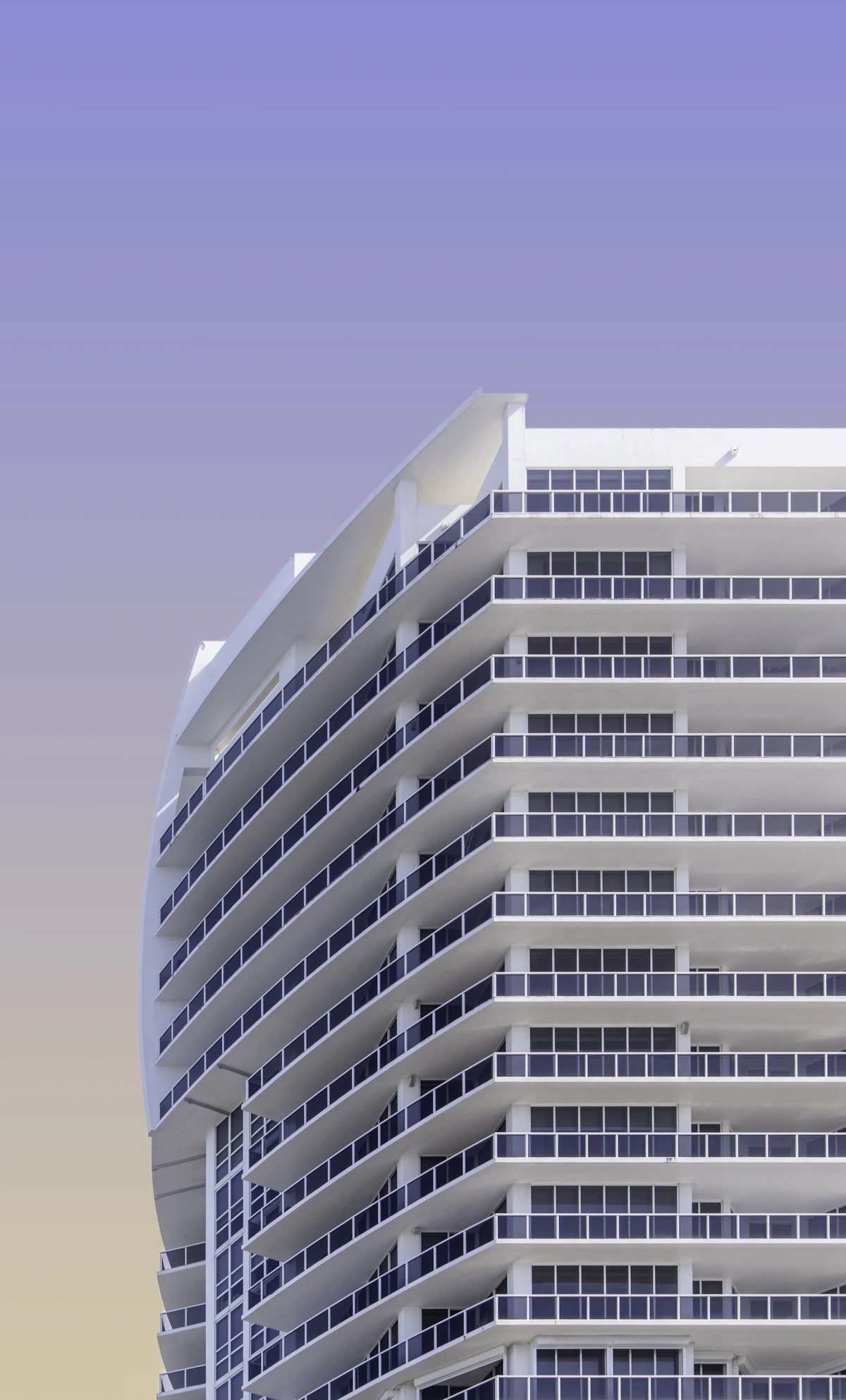 Curved white high-rise condominium with rows of balconies against a pale sky