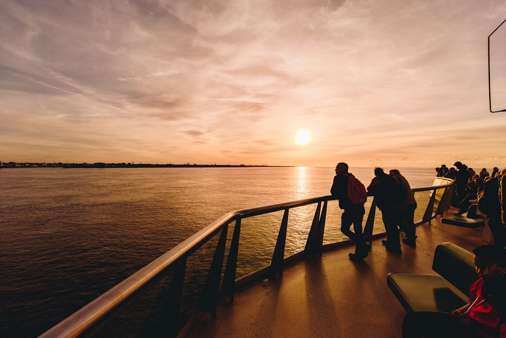 silhouette of 2 men and woman standing on wooden dock during sunset