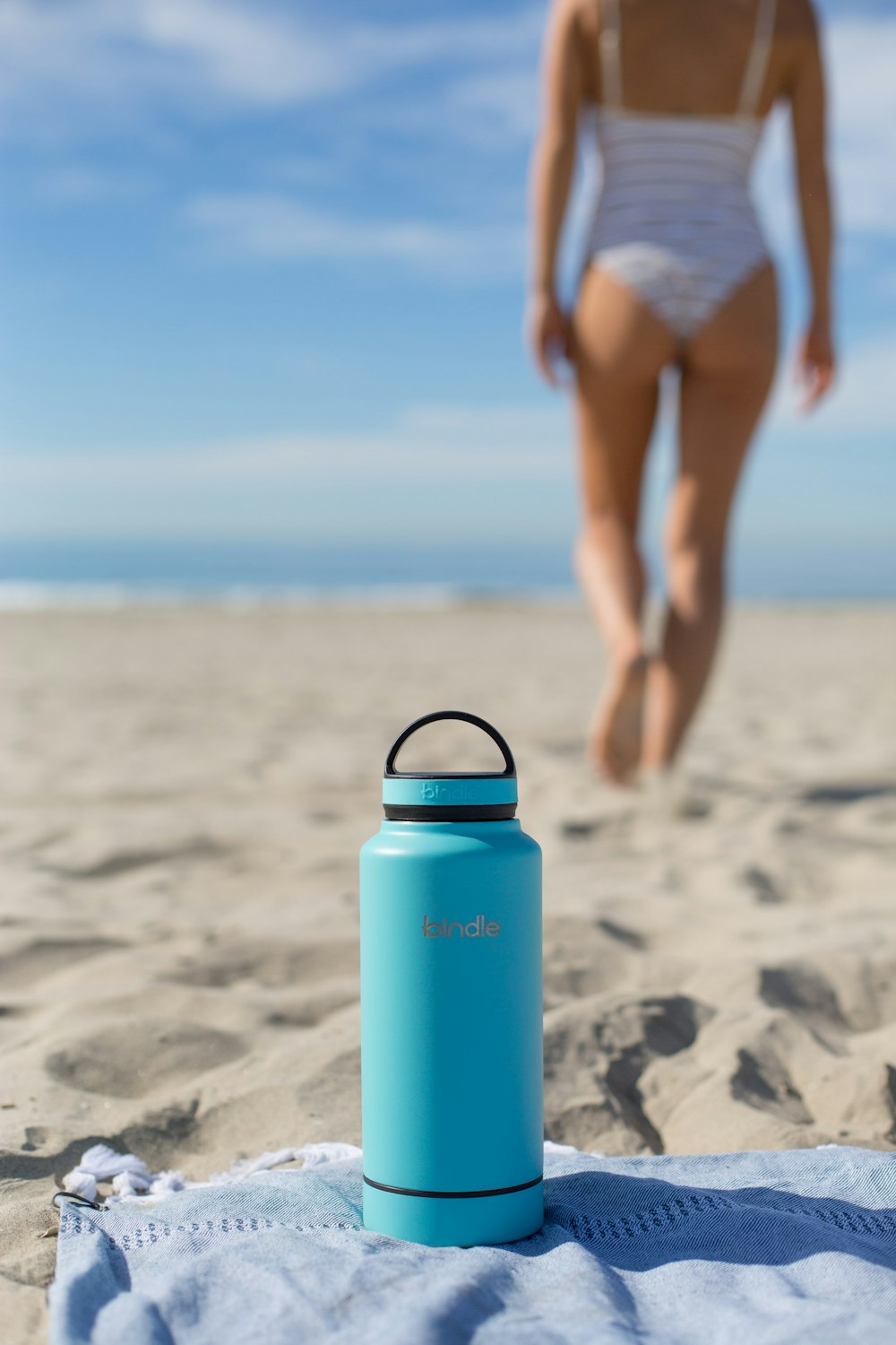 woman in white bikini bottom holding blue and black thermal carafe on beach during daytime