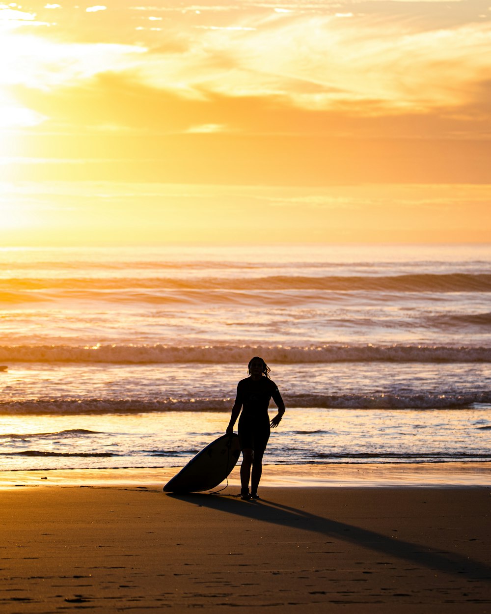 Silhouette einer Frau, die während des Sonnenuntergangs am Strand spazieren geht