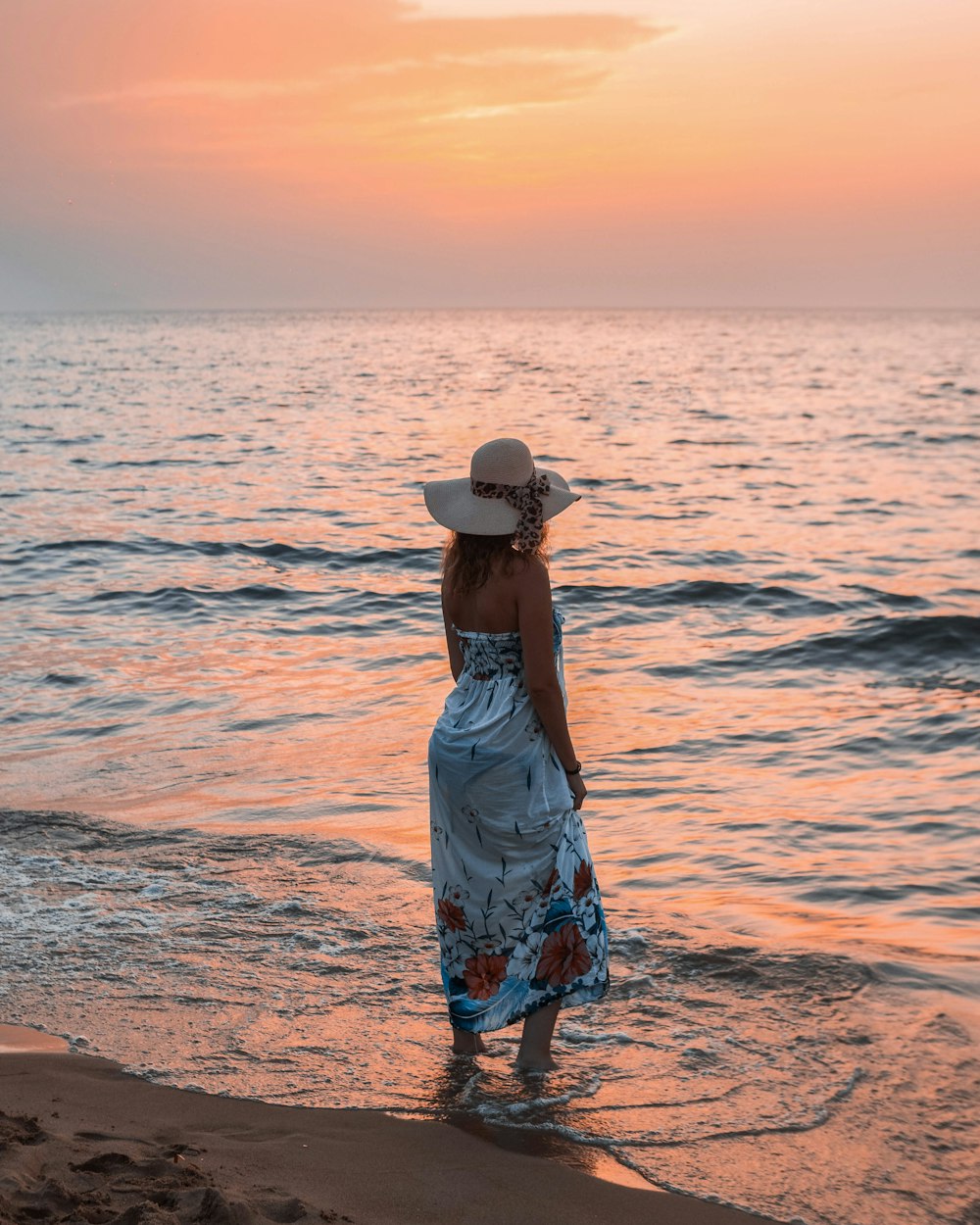 Mujer en vestido floral azul y blanco de pie en la playa durante el día