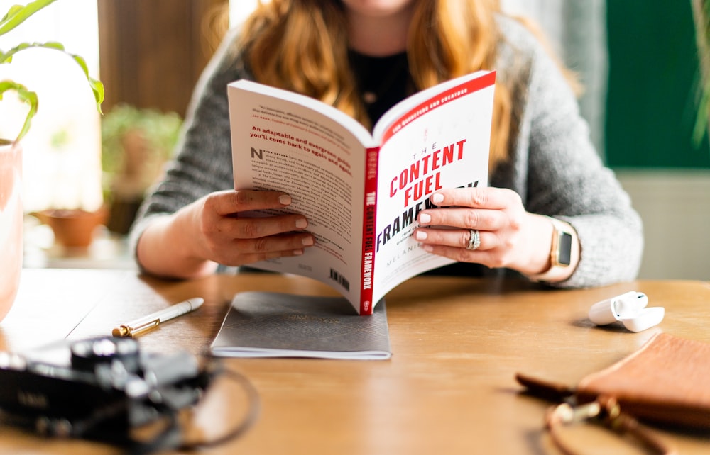 woman in gray sweater holding white and red book