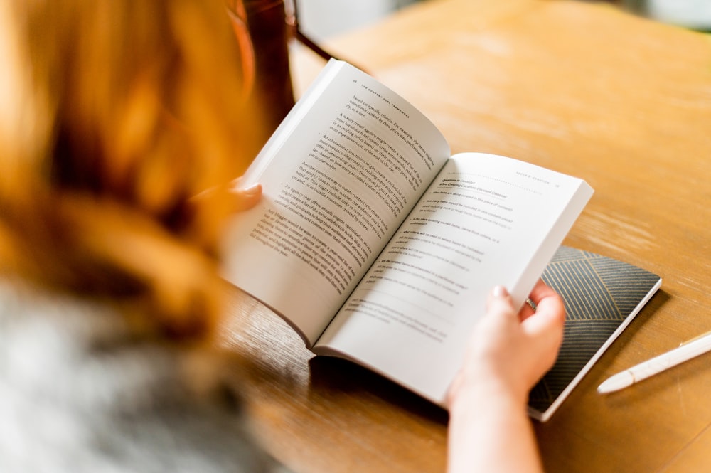 person reading book on brown wooden table