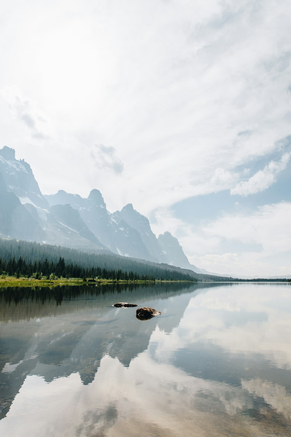 lake near green trees and mountain under white clouds during daytime