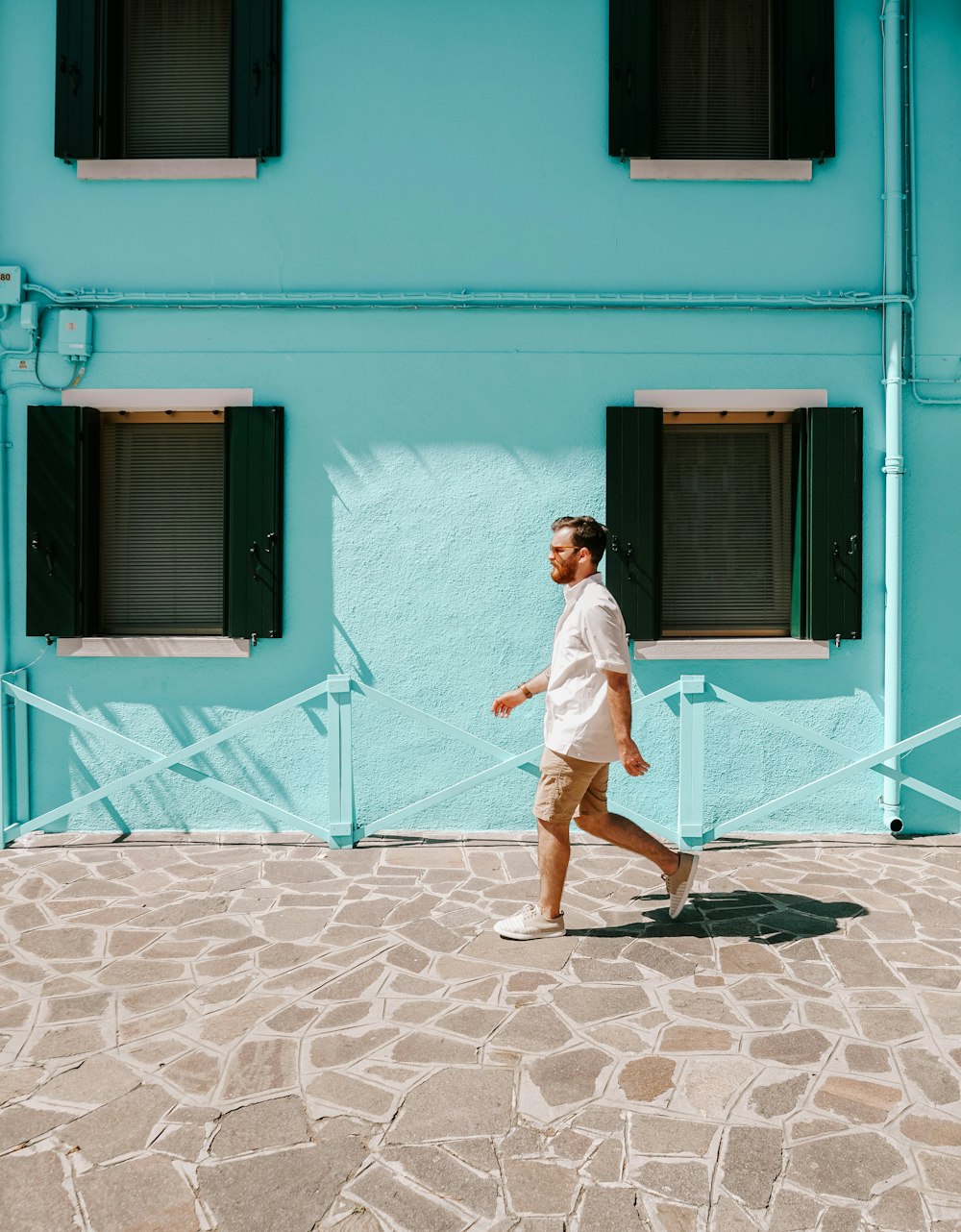 man in white dress shirt and brown shorts standing in front of blue concrete building during