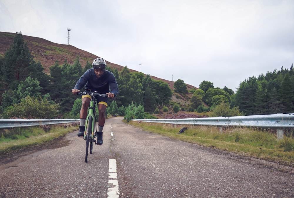 Un homme en chemise verte fait du vélo sur une route en béton gris pendant la journée