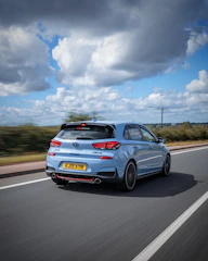 Side profile of a blue compact hatchback with modern curves on a coastal road.