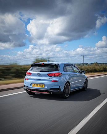 A vibrant blue Hyundai i20 cruising along a coastal highway with ocean views.