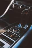 A close-up view of a car's central console featuring a gear shift and various control buttons, including one labeled 'AUTO.' The design is sleek and modern, with metallic and black elements.