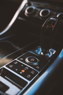 A close-up view of a car's central console featuring a gear shift and various control buttons, including one labeled 'AUTO.' The design is sleek and modern, with metallic and black elements.