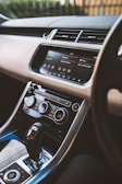 A modern car interior showcasing a sleek dashboard with a touchscreen infotainment system displaying media and phone options. There are various control dials for air conditioning and other functions, along with a gear shift lever in the foreground.