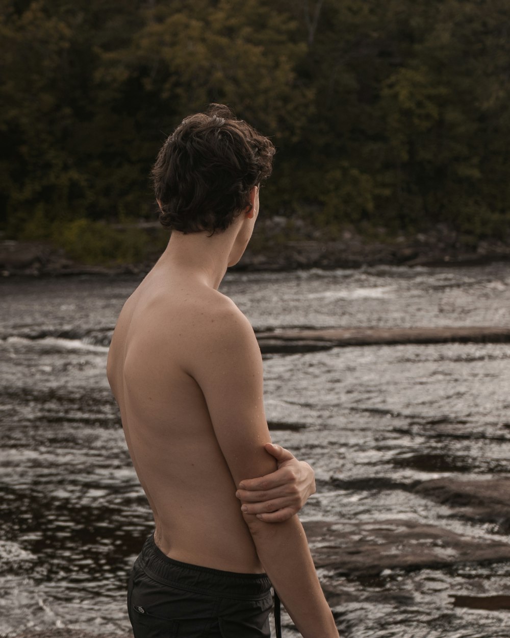 topless boy in black shorts standing on brown sand near body of water during daytime