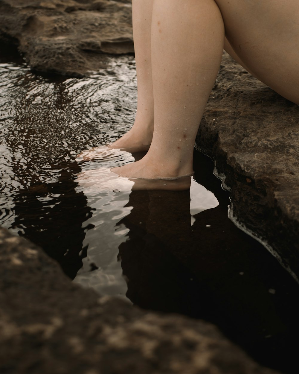 person in black shorts sitting on rock