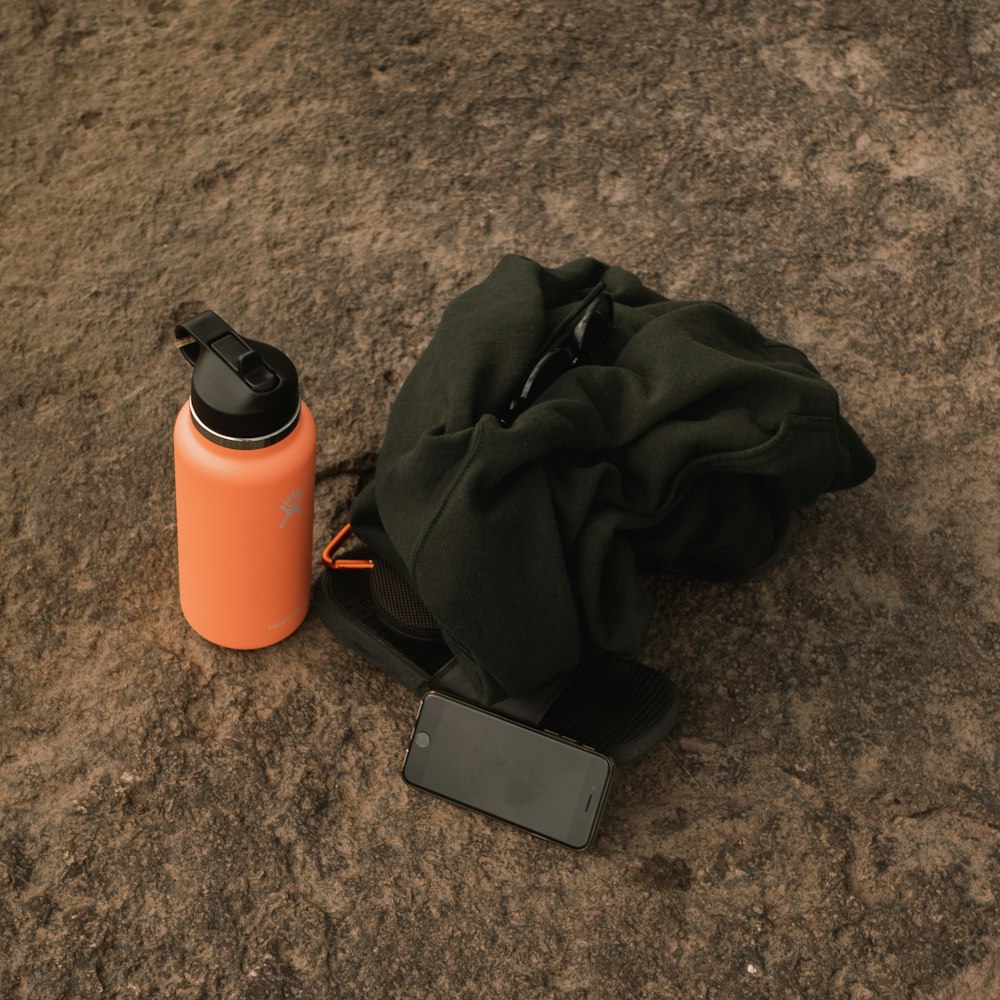 black smartphone beside orange and black tumbler