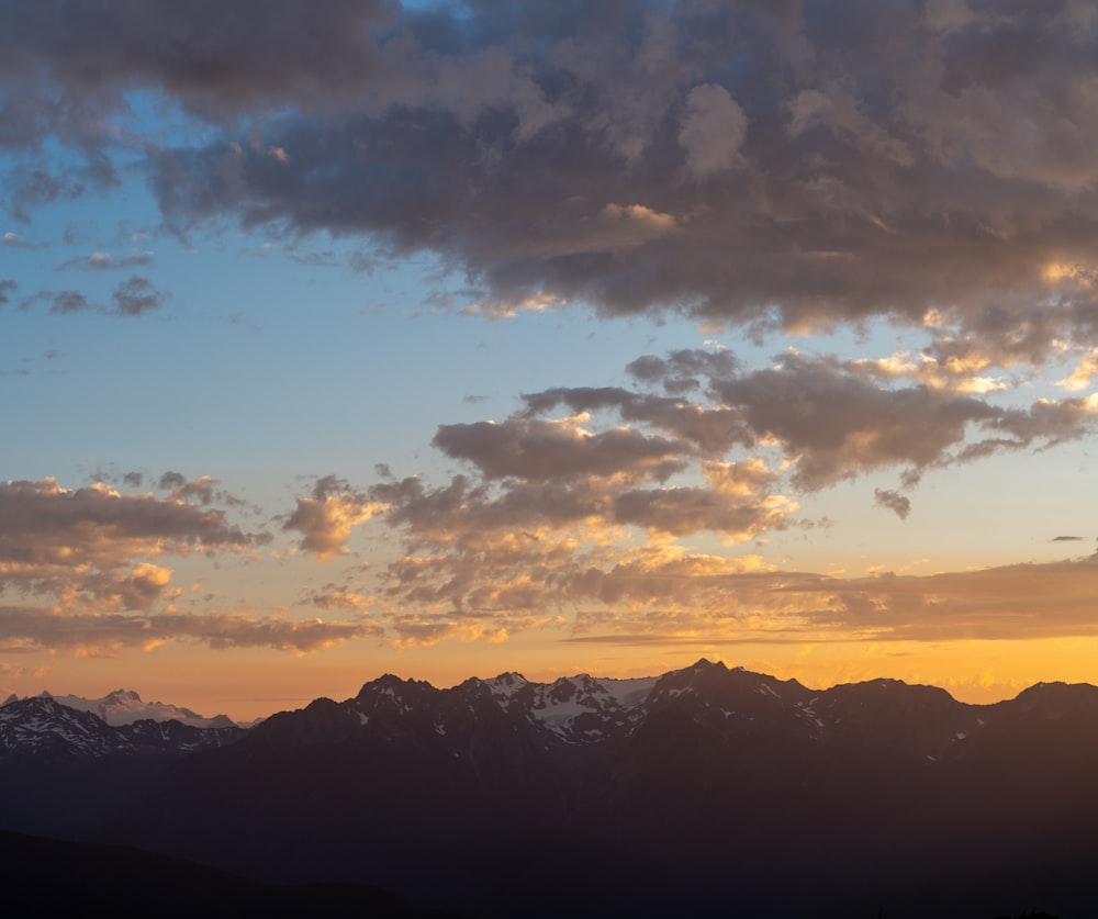 silhouette of mountains under cloudy sky during sunset