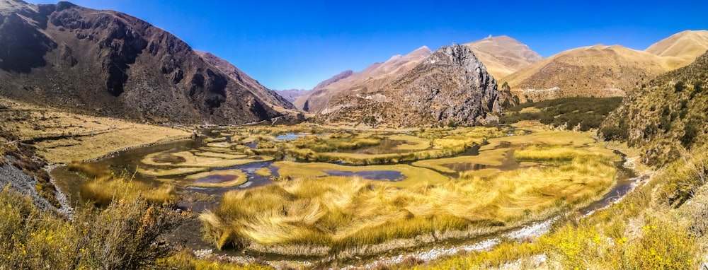 green grass field near mountain under blue sky during daytime