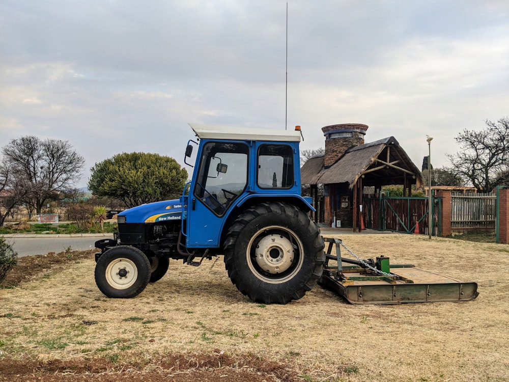 blue tractor on green grass field near brown wooden house under white clouds during daytime