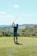 A golfer practicing their swing on a lush green golf course under a clear blue sky.