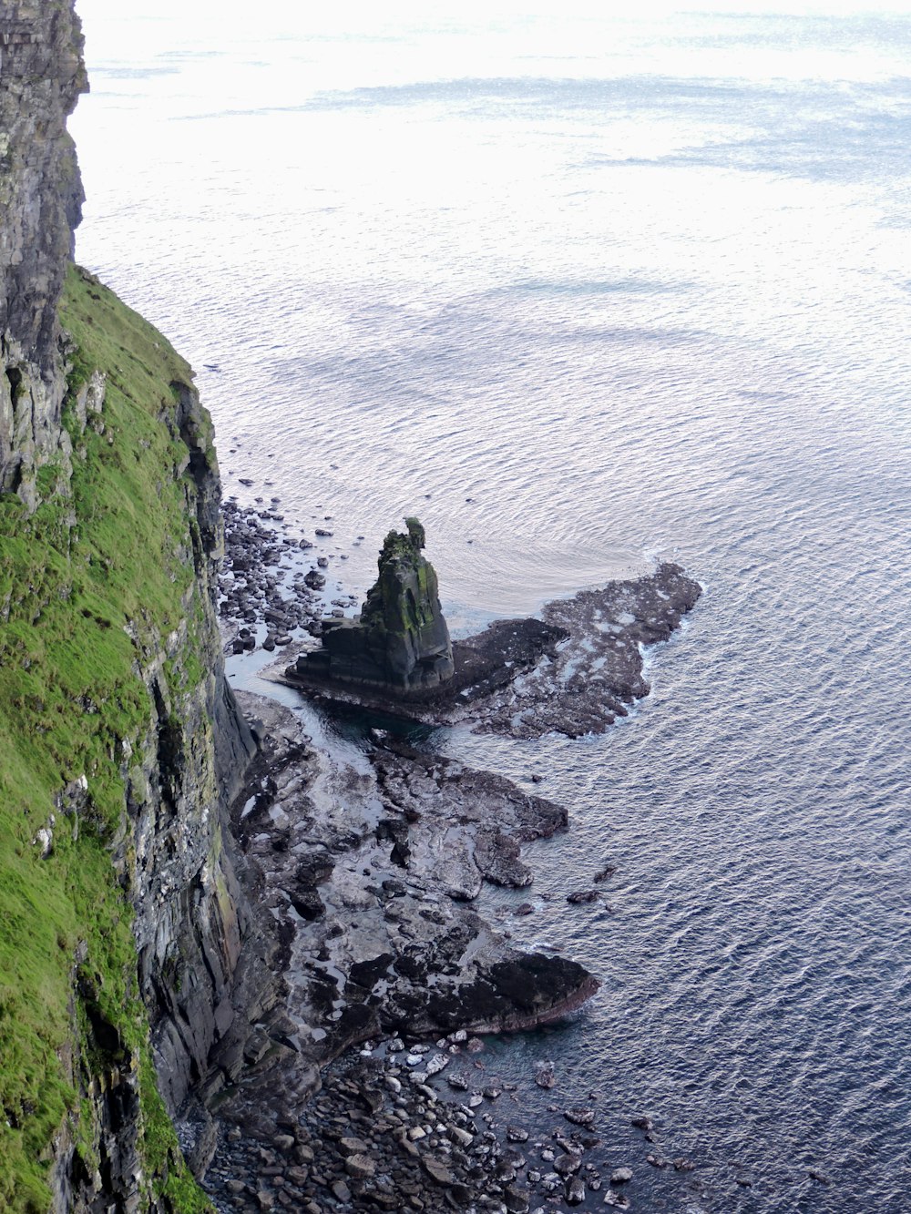 green and black rock formation beside body of water during daytime