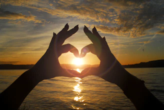 silhouette of person doing heart hand sign during sunset