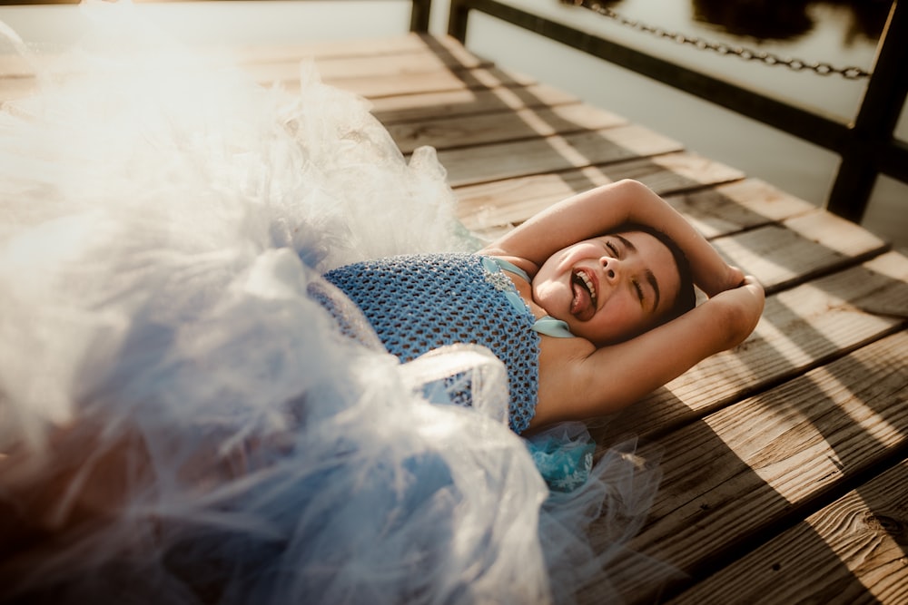 girl in blue and white polka dot shirt lying on brown wooden floor